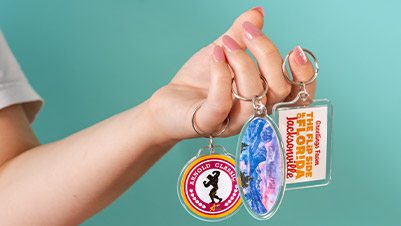 A Hand with Round, Oval and Rectangle Acrylic Keychains Hanging from the Fingers