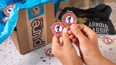 Hands holding round keychains promoting Arnold Classic