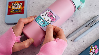 A Child's Hands Applying a Square Hello Kitty Sticker to a Water Bottle