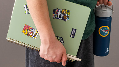 A Student with MLH Stickers on Notebook and Adam Savage Circle Sticker on Water Bottle